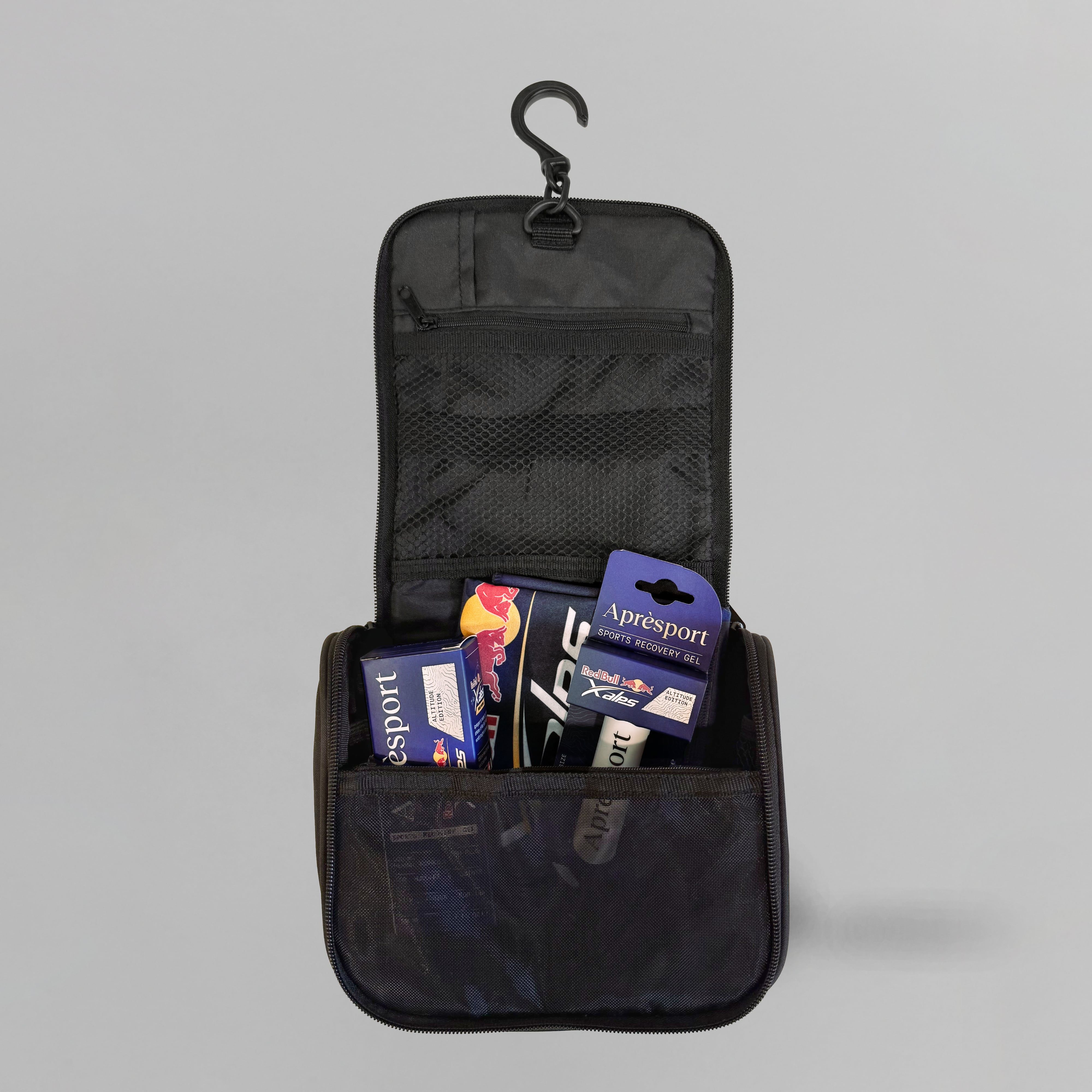 Black travel toiletry bag with hanging hook, containing travel-sized products on a gray background